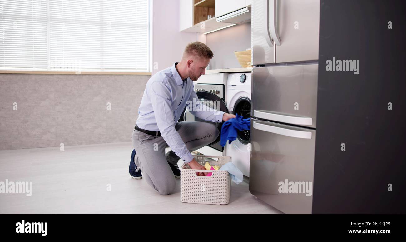 Young Man Loading Clothes Into Washing Machine In Kitchen Stock Photo