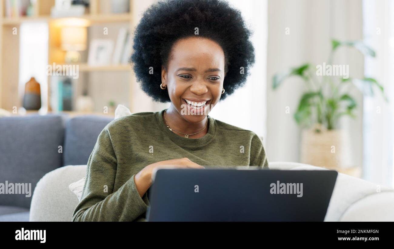 Female with an afro enjoying a comedy movie on her laptop while eating a big bowl of popcorn at home. African woman laughing while watching funny Stock Photo