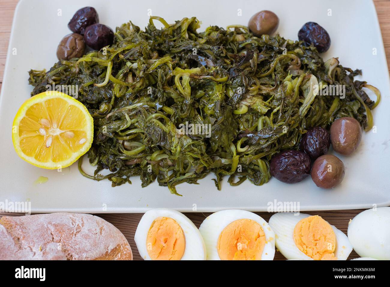 boiled wild greens, dandelion, lemons and extra virgin olive oil, on a wooden table. Horta or Wild Greens. Greek Cuisine. Stock Photo