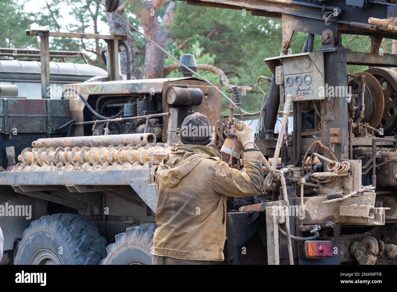 Team of workers with drilling rig on car are drilling artesian well for