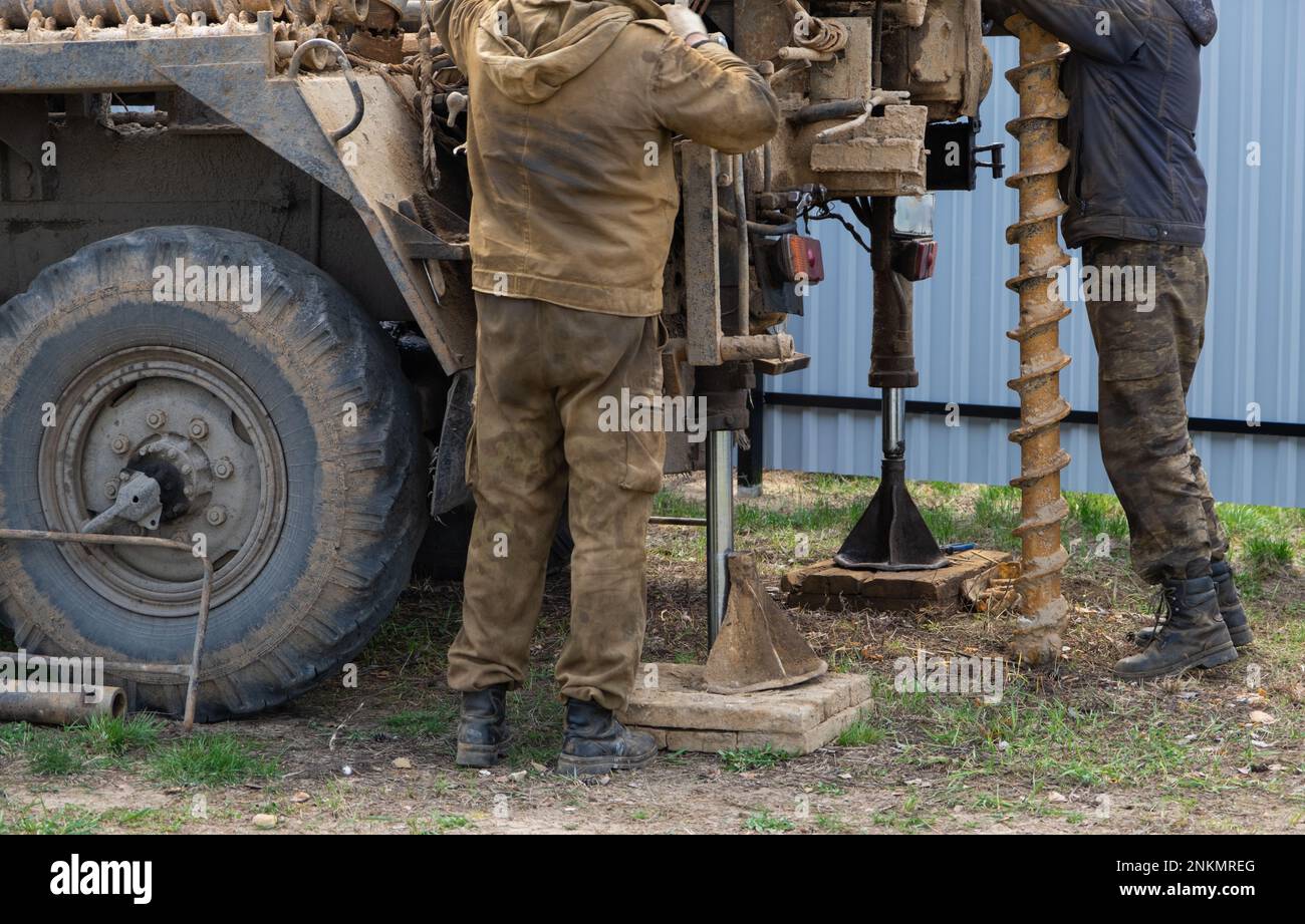Team of workers with drilling rig on car are drilling artesian well for