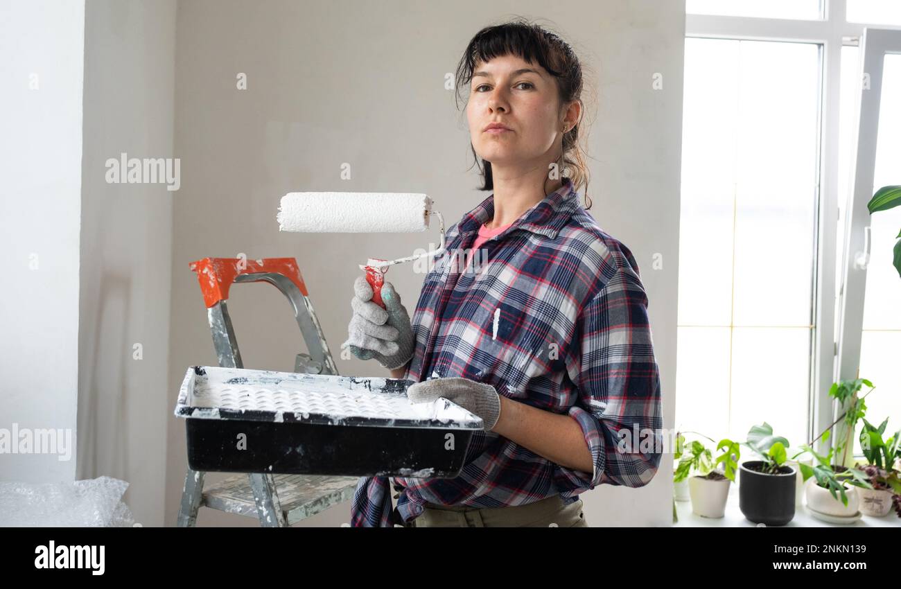 puzzled woman in paint roller and white paint for walls in hands close