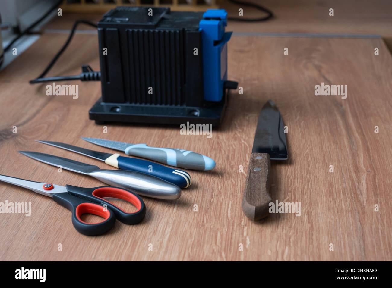 Sharpening a knife on an electric sharpener at home. Flatlay knife blade, scissors, sharpeners, dust flies on the machine. Stock Photo