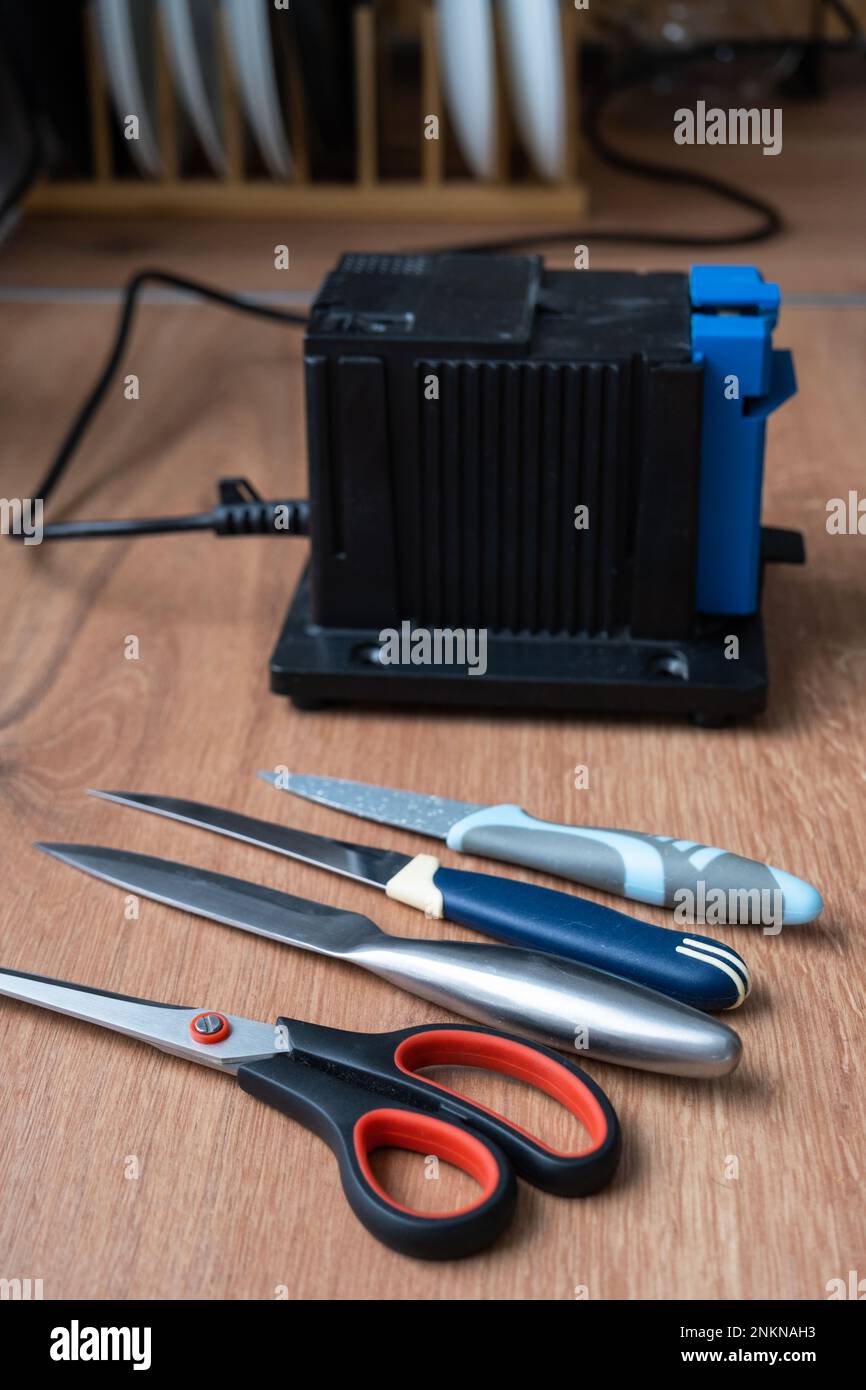 Sharpening a knife on an electric sharpener at home. Flatlay knife blade, scissors, sharpeners, dust flies on the machine. Stock Photo