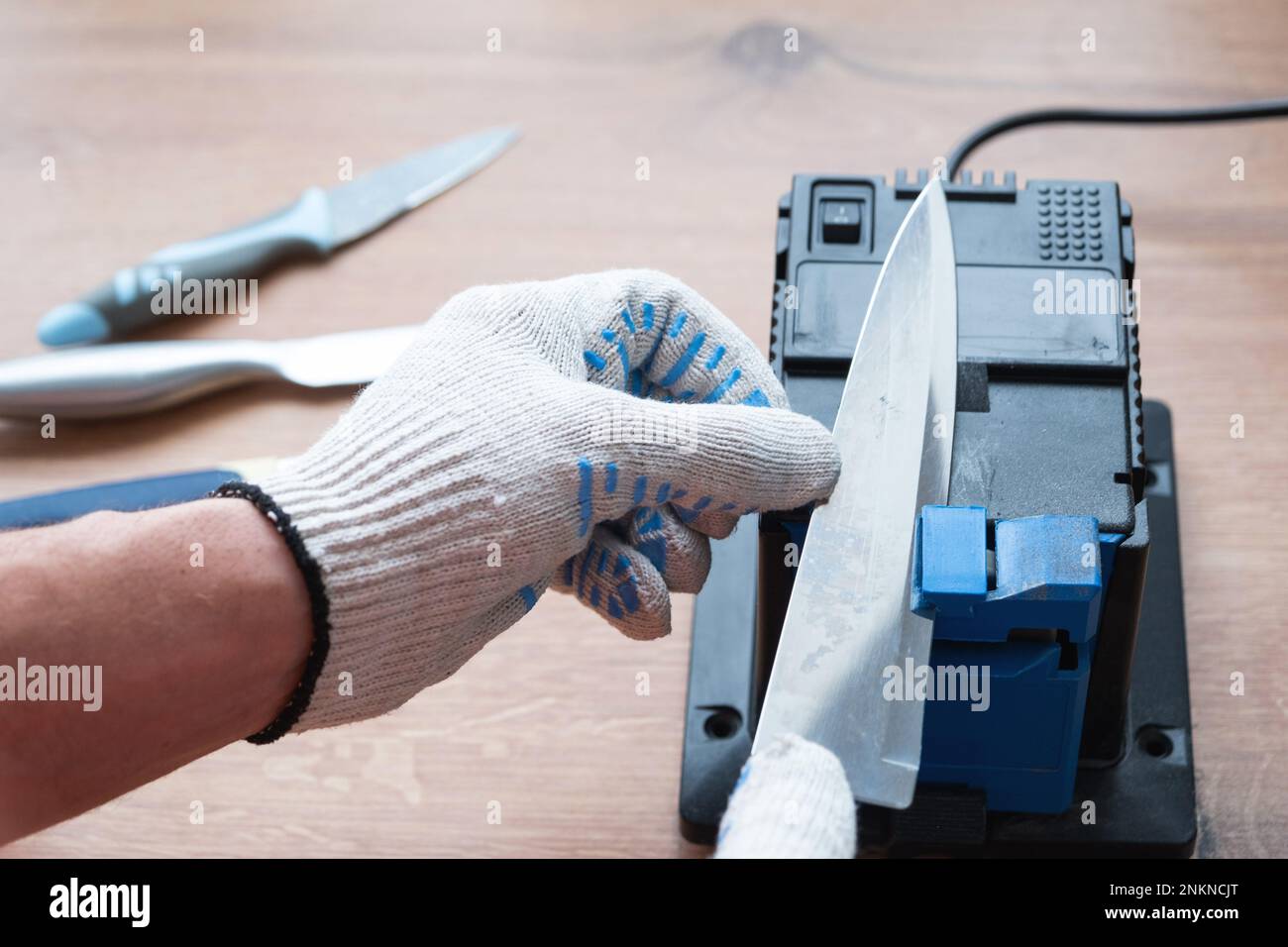 Sharpening a knife on an electric sharpener at home. The man's hand