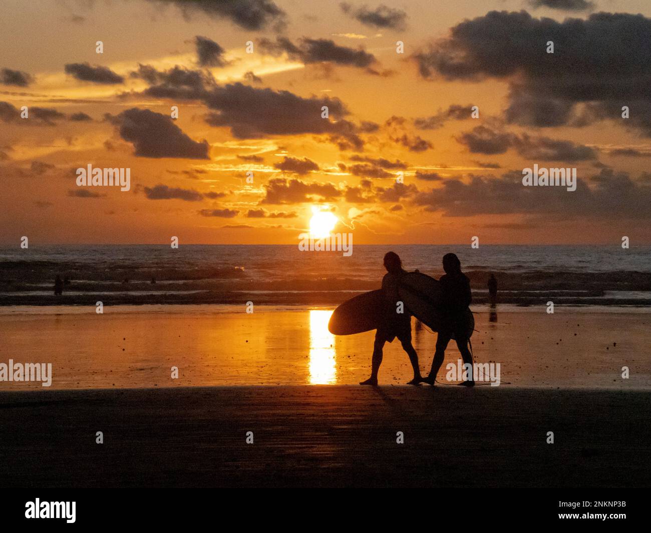Two surfers in silhouette return from the water at sunset in Nosara in Costa Rica Stock Photo