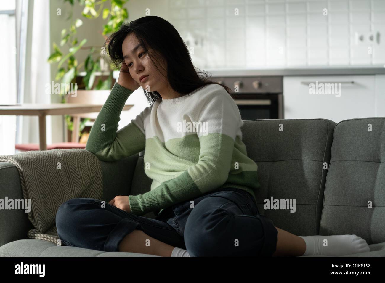 Anxious Asian millennial girl sitting on sofa alone feeling lonely, suffering from monophobia Stock Photo