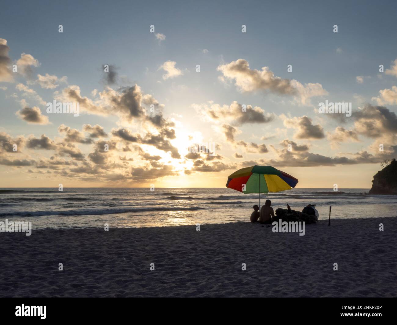 A family enjoys the last of the sun under the shade of a colourful umbrella on a beach near Nosara in Costa Rica Stock Photo