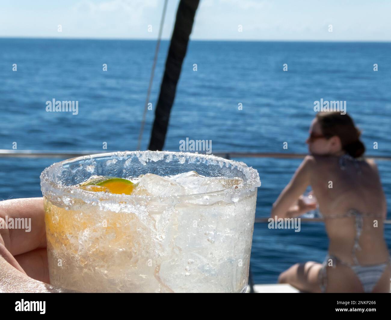 A margarita with salt on the rim on a boat with a woman in the background in Costa Rica Stock Photo