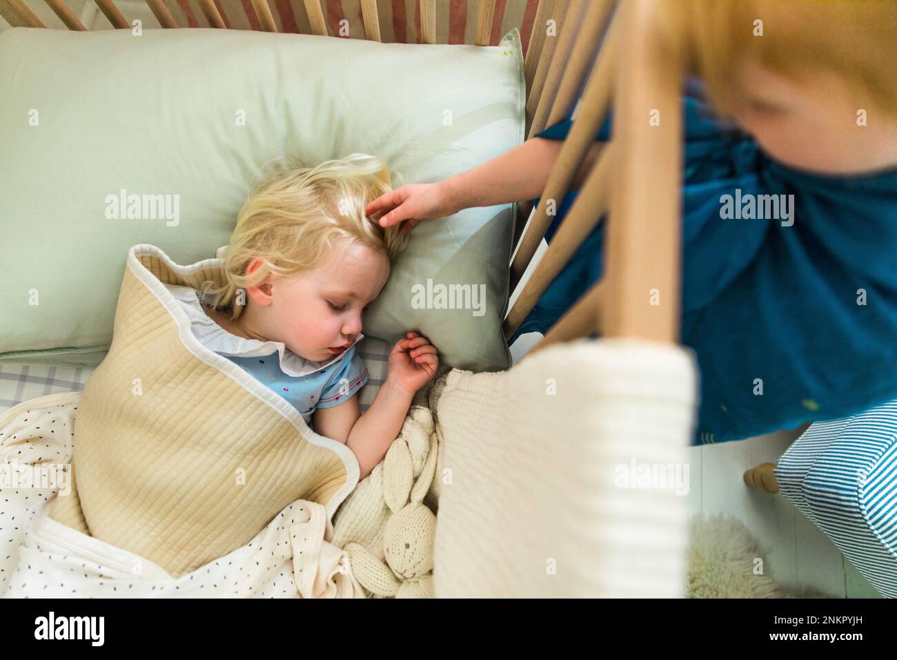 Young girl in cot with sibling stroking her hair Stock Photo