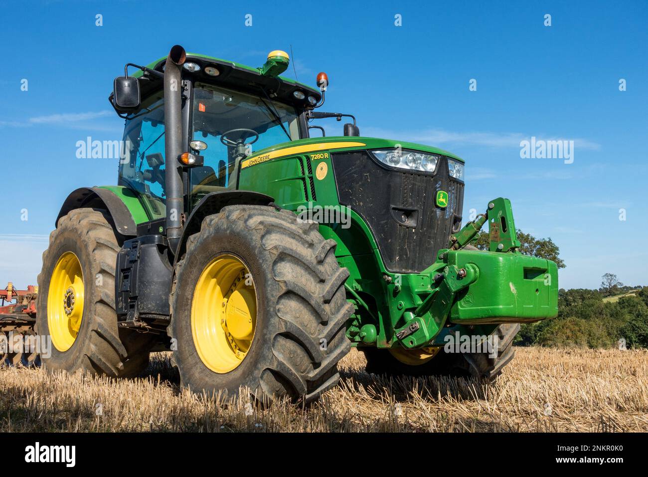 Large, bright green, John Deere 7280R row crop farm tractor with big fat tyres and with disk harrow behind parked in Leicestershire field, England, UK Stock Photo
