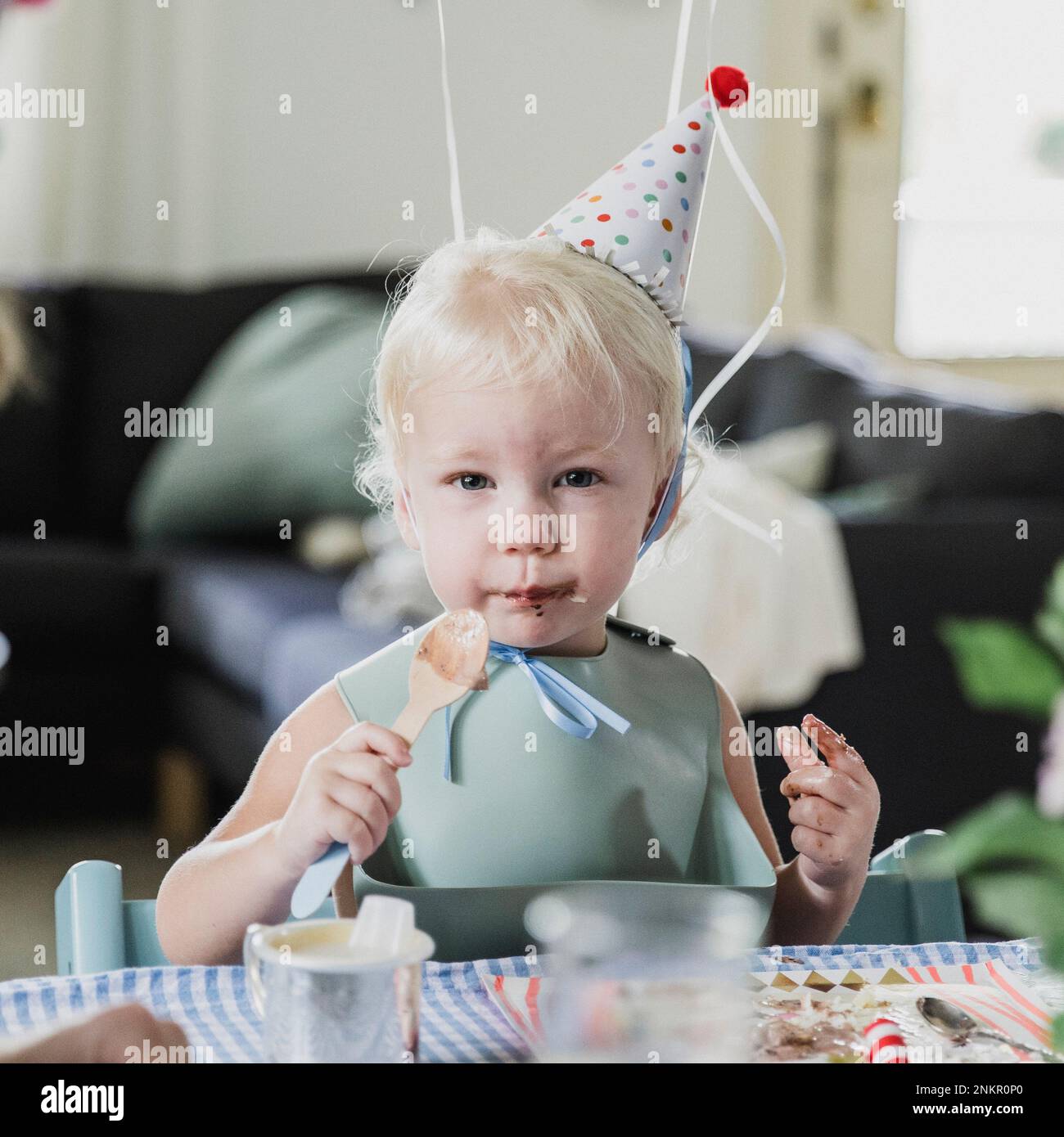 Young girl eating food with spoon and wearing party hat Stock Photo Alamy