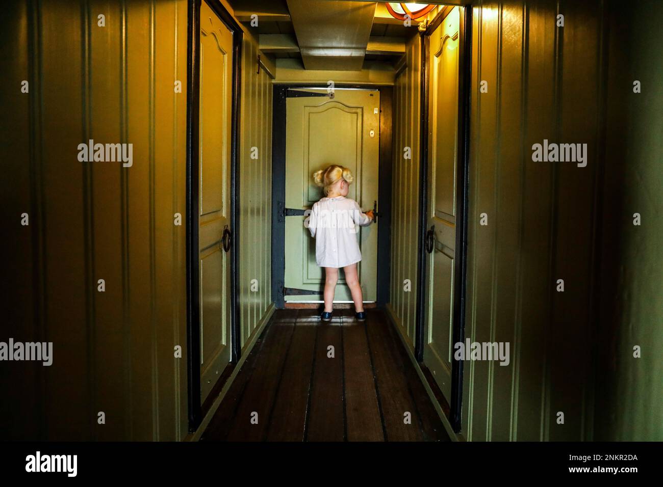 Girl standing at end of corridor in front of closed door Stock Photo
