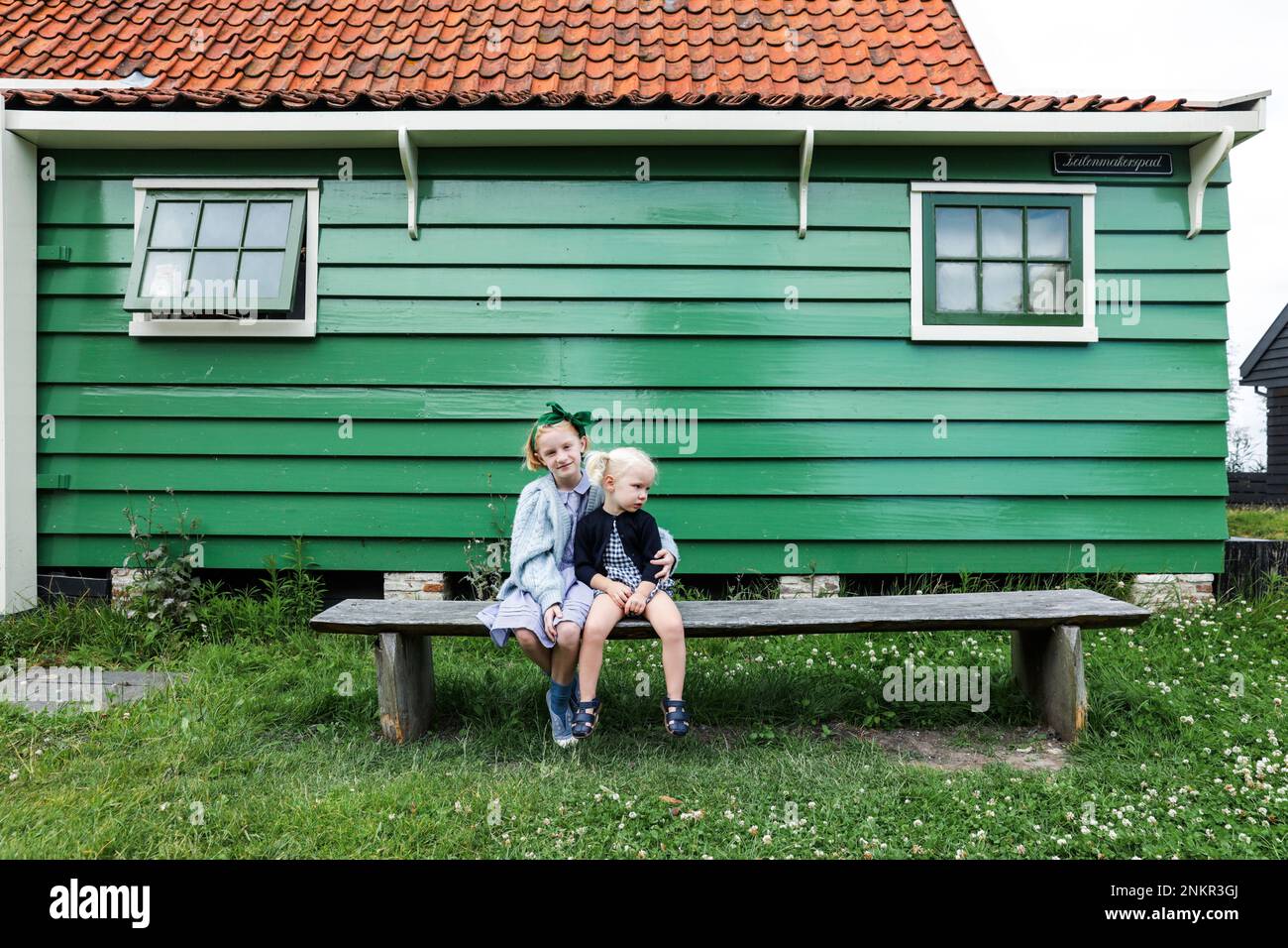 Two girls outside wooden house sitting on bench Stock Photo - Alamy