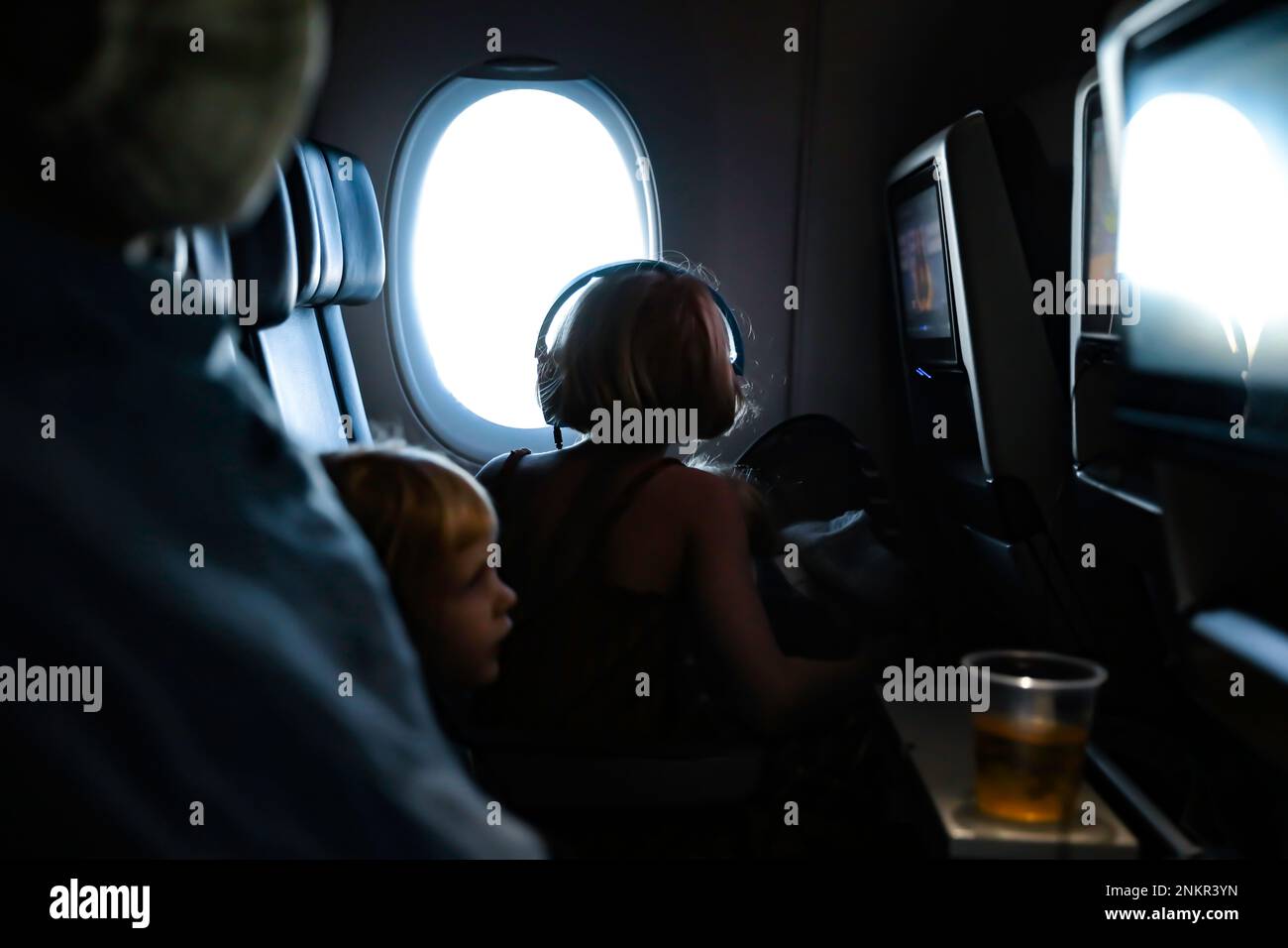 Child sitting by window on plane looking out wearing headphones Stock