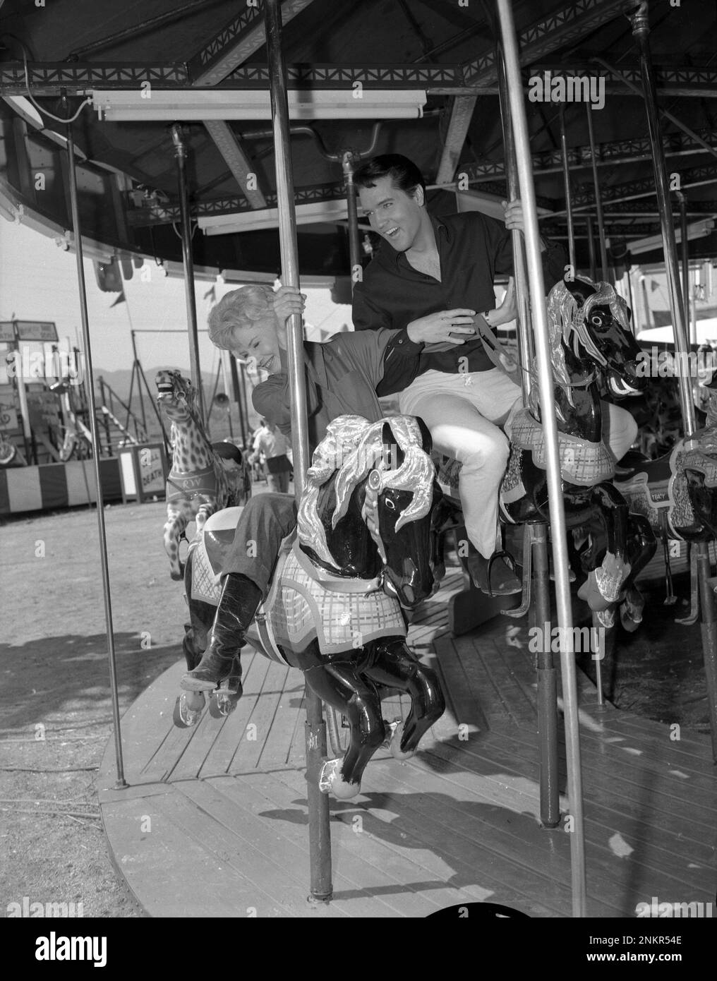 Barbara Stanwyck and Elvis Presley riding a merry-go-around at the set of Roustabout, 1964 Stock Photo