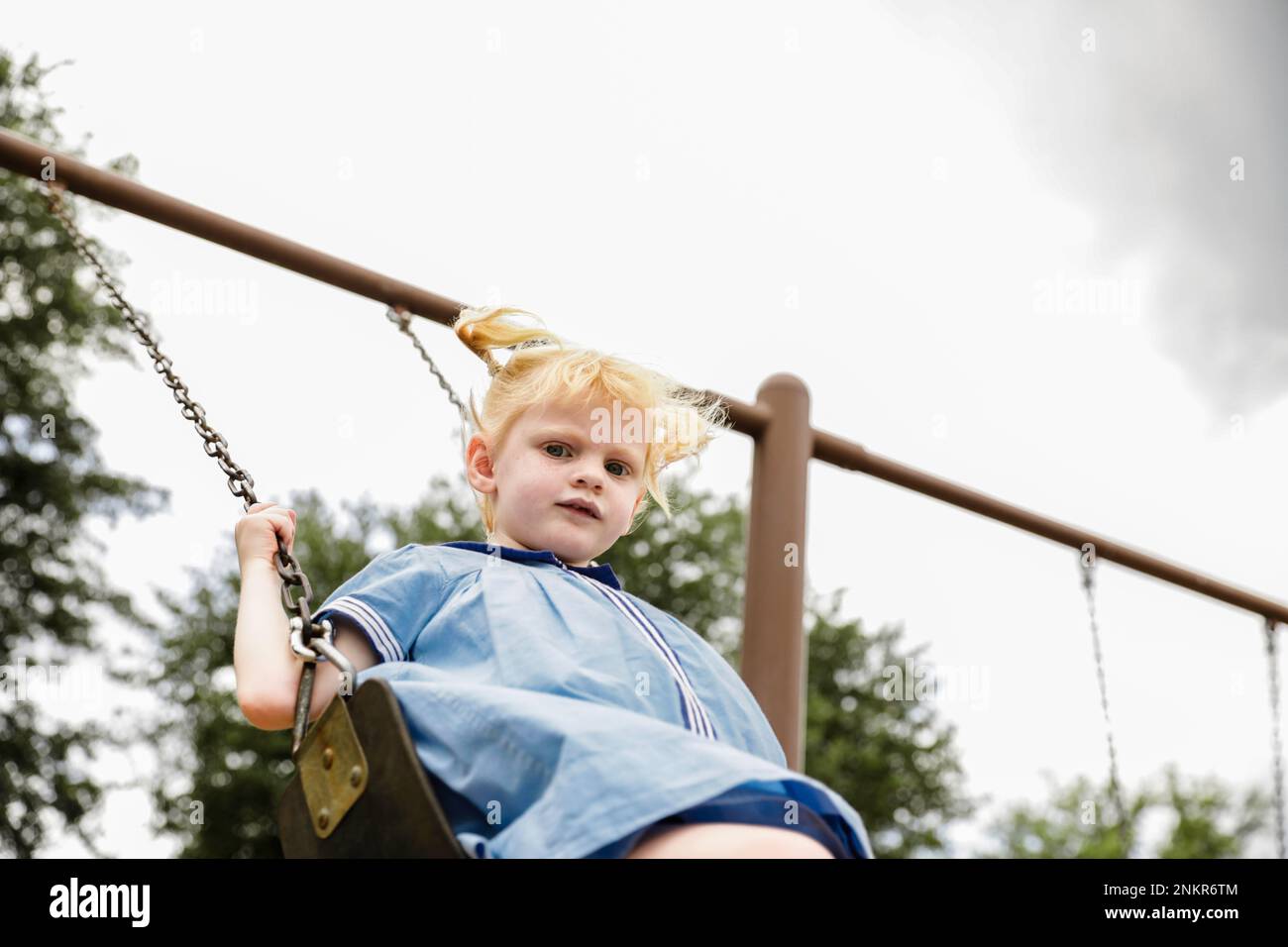 Girl swinging on swing in play park Stock Photo