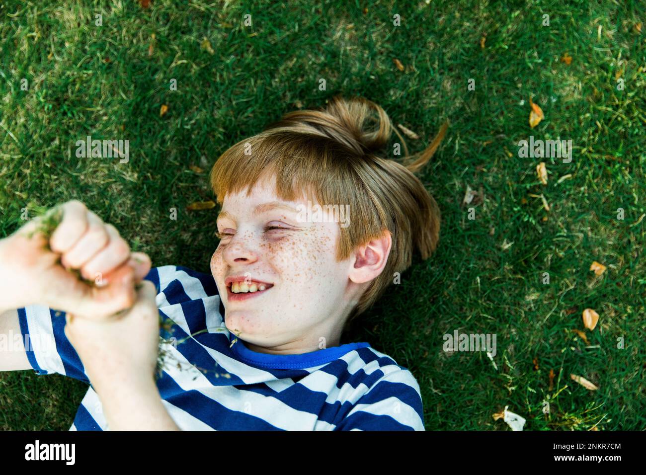 Boy with freckles lying on grass, smiling Stock Photo