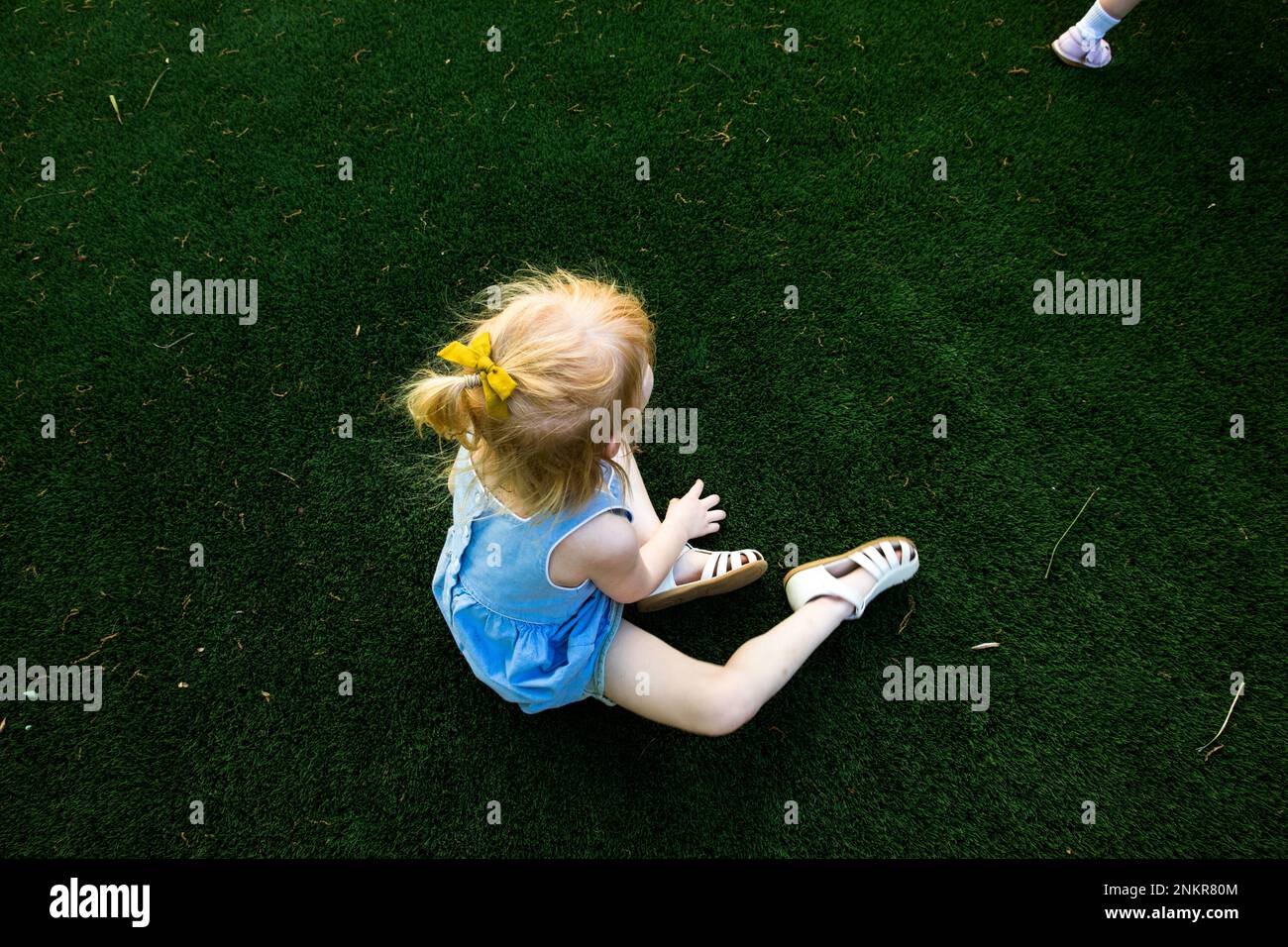 Overhead view of young girl sitting on grass wearing sandals Stock Photo