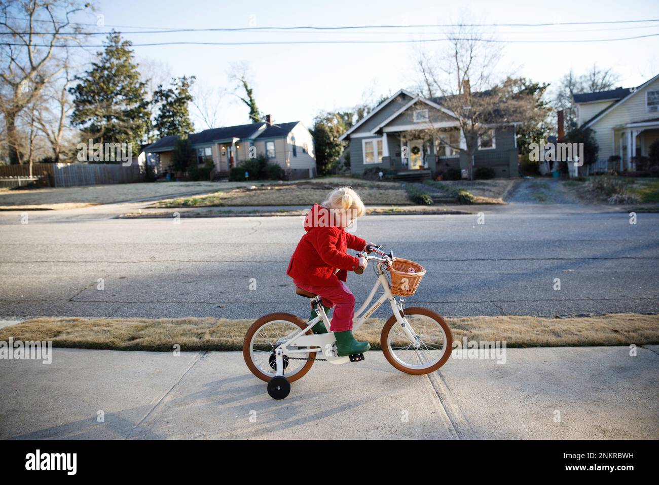 Girl wearing red coat riding bicycle along sidewalk Stock Photo