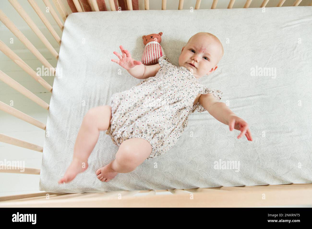 Overhead view of baby girl wearing babygro lying in crib Stock Photo