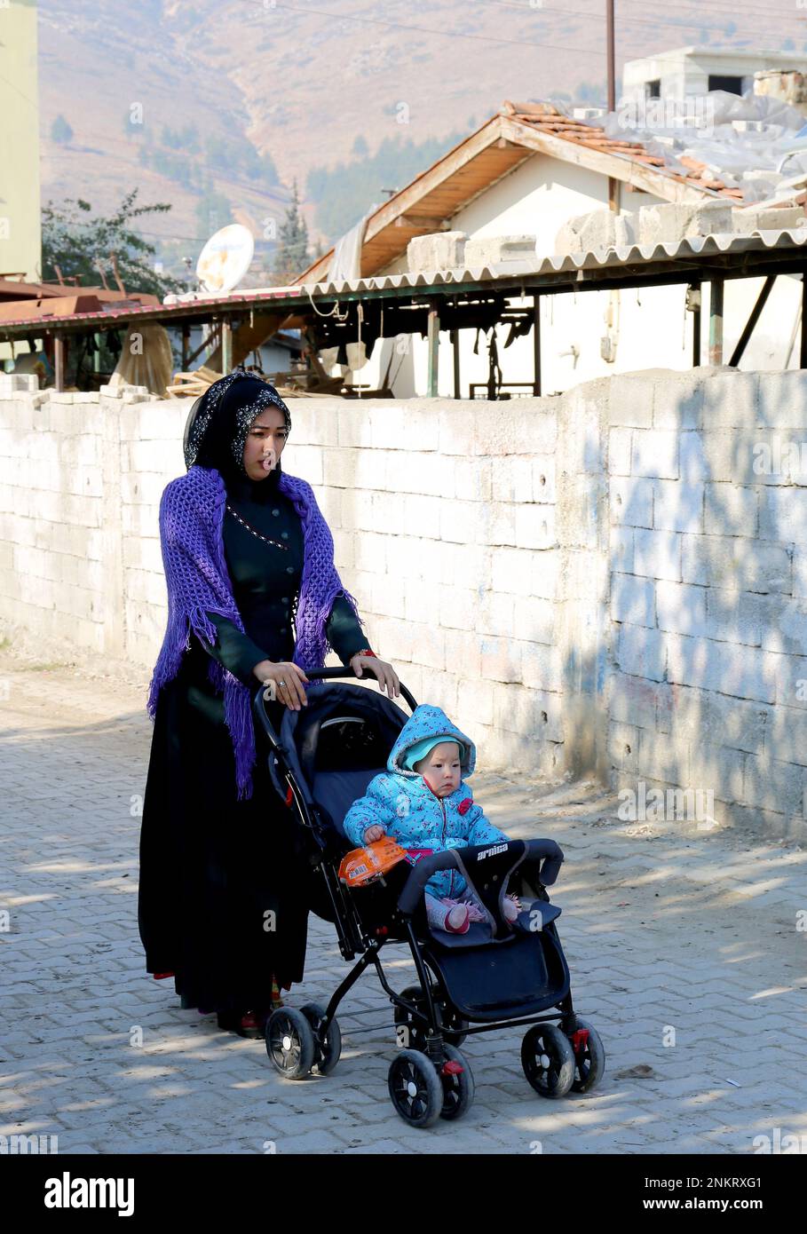 OVAKENT,HATAY,TURKEY-DECEMBER 10:Unidentified Uzbek Woman with son on Stroller walking down the street. December 10,2016 in Ovakent, Hatay, Turkey Stock Photo