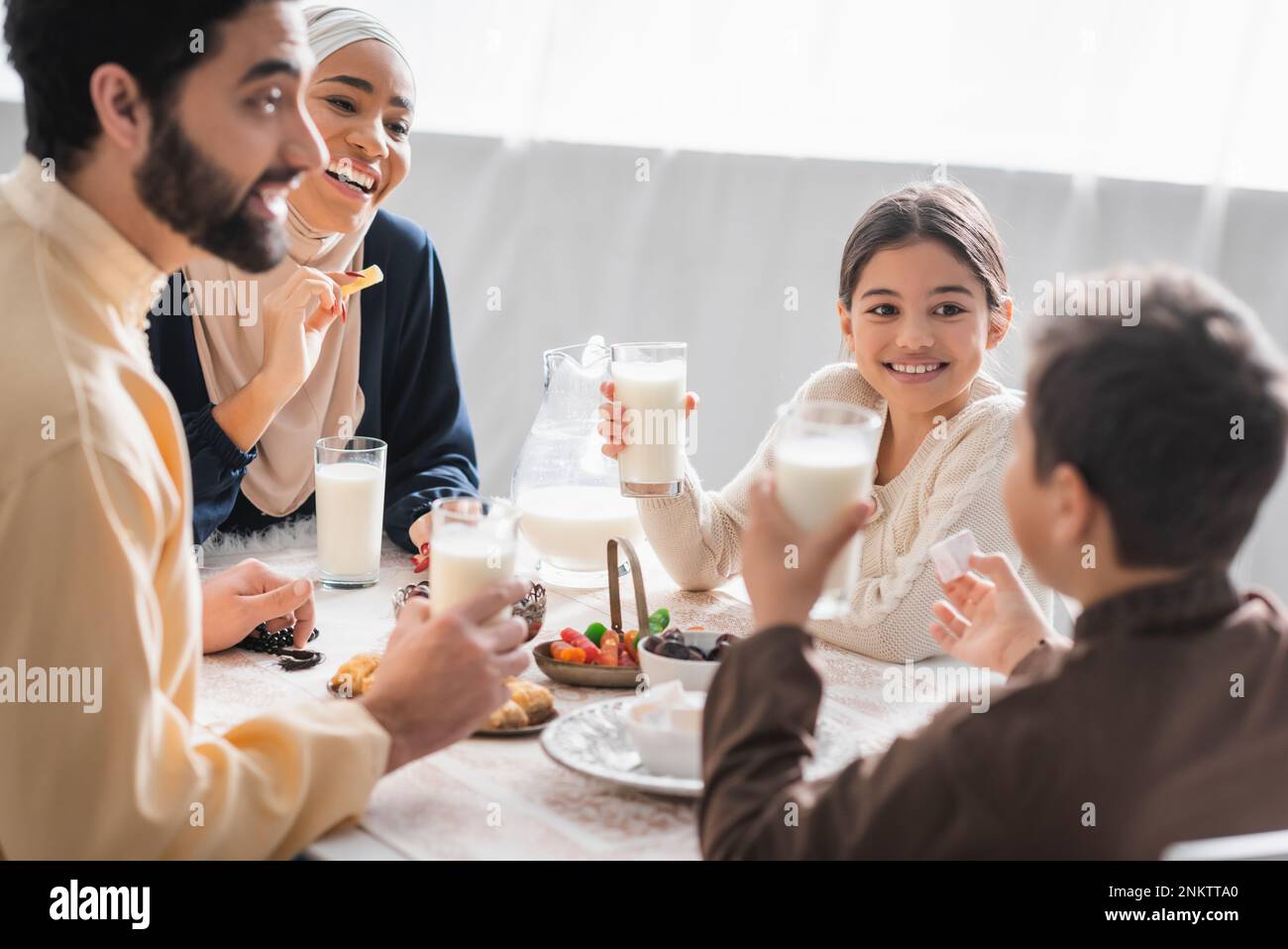 Positive muslim family holding glasses of milk and talking near food during suhur at home,stock image Stock Photo