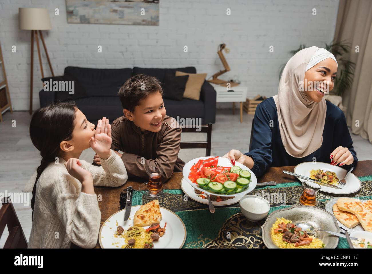 Cheerful muslim kids talking near african american mom in hijab during iftar at home,stock image Stock Photo