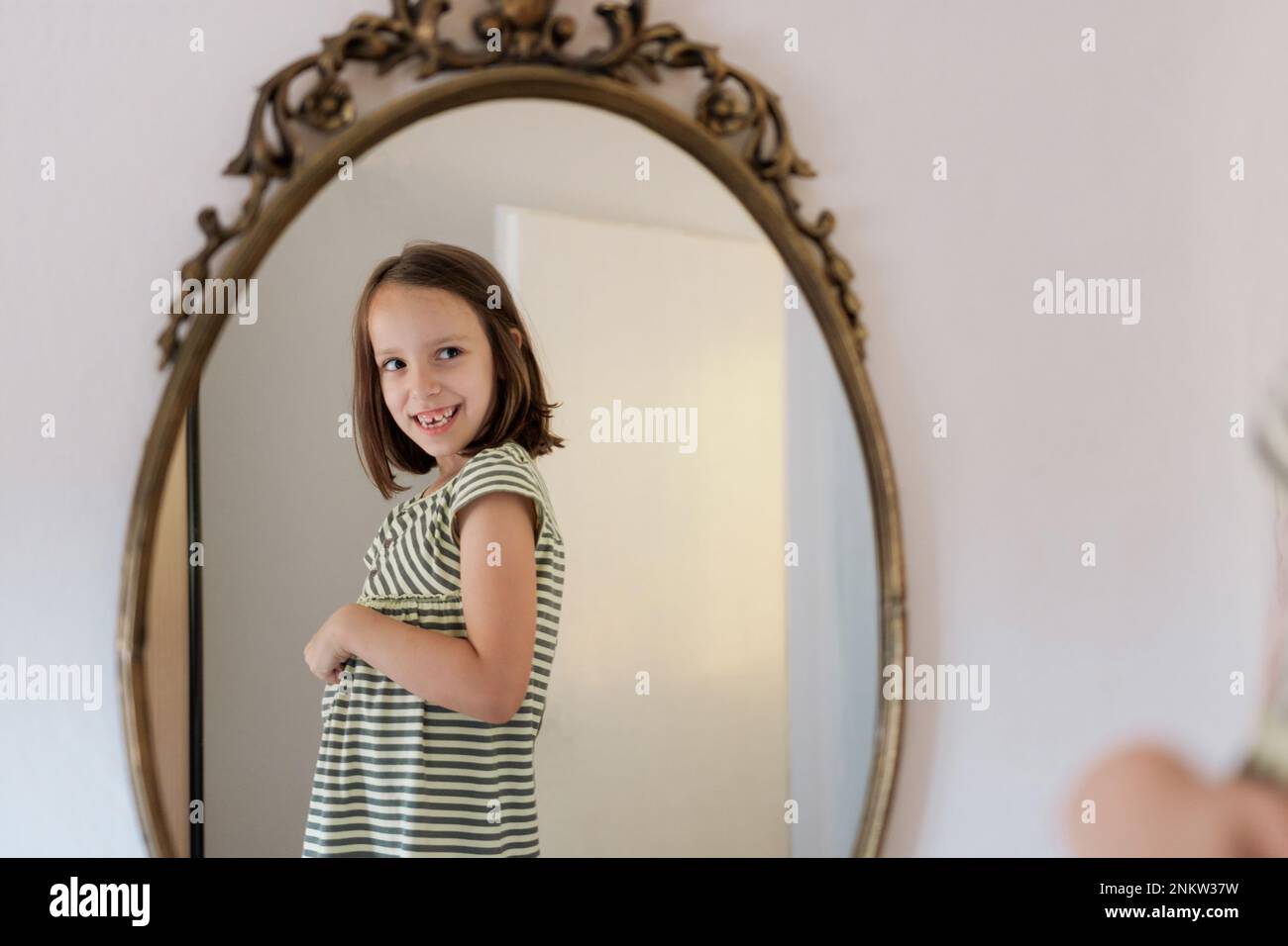 Happy little girl is standing in front of a mirror at home Stock Photo