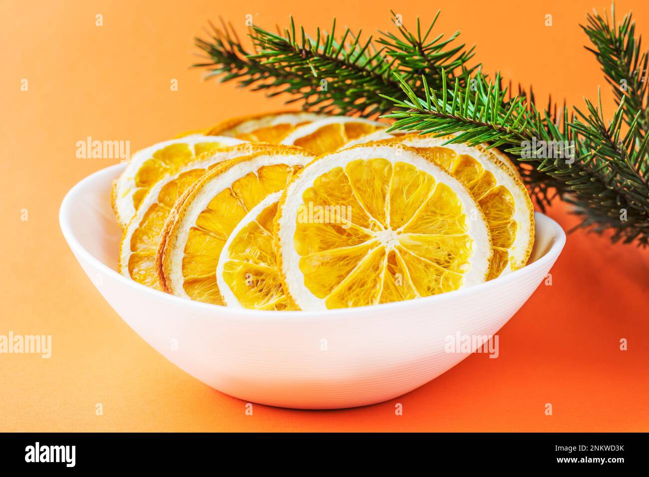 Orange chips in a white plate, near the spruce branch, on an orange red background. Eco organic homemade dried orange slices, chips. Healthy snack. Cl Stock Photo