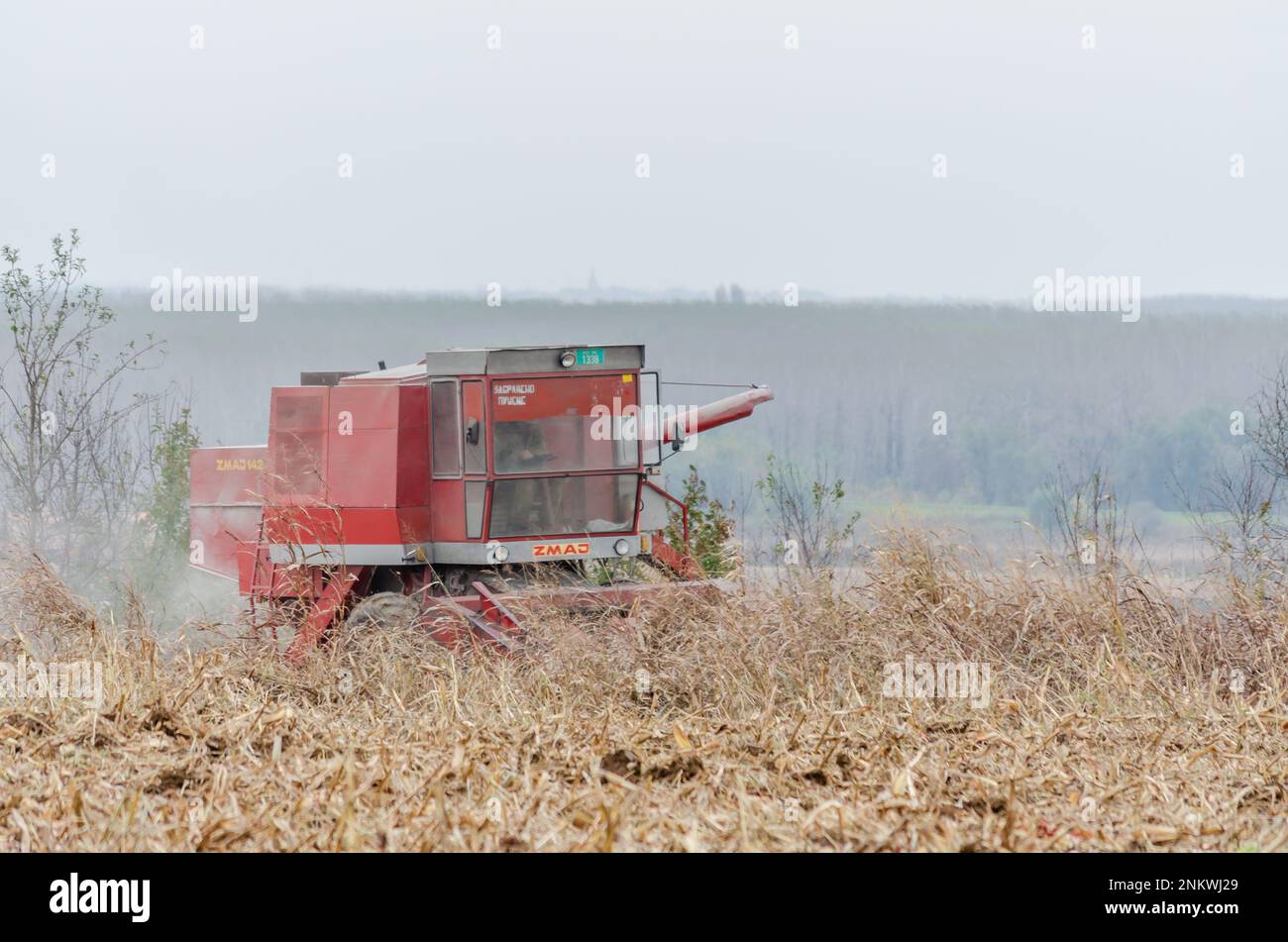 A tractor is seen plowing a field, churning up soil and weeds in the process Stock Photo