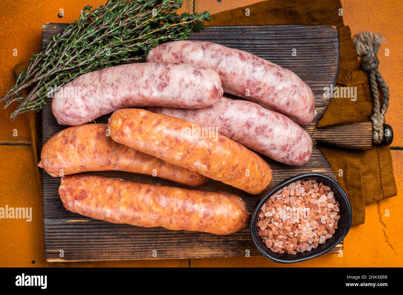 Fresh Raw Bratwurst and Chorizo meat sausages on wooden board. Orange background. Top view. Stock Photo