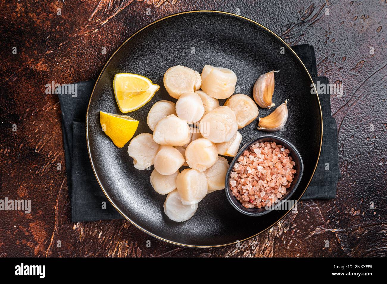 Raw sea scallops seafood on a plate with pink salt and lemon. Dark background. Top view. Stock Photo