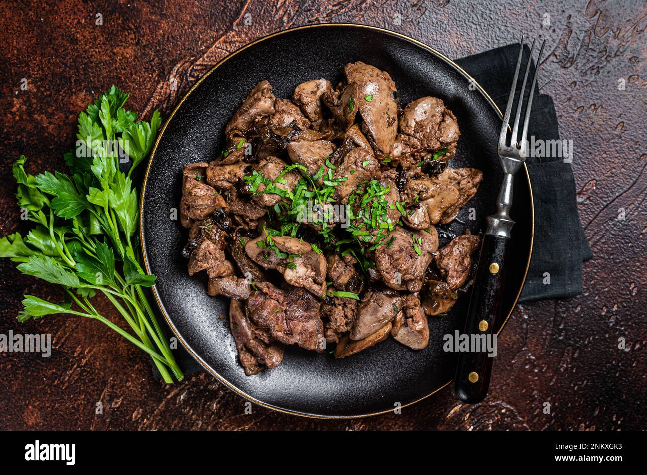 Fried chicken liver with onions and parsley in a plate. Dark background. Top view. Stock Photo