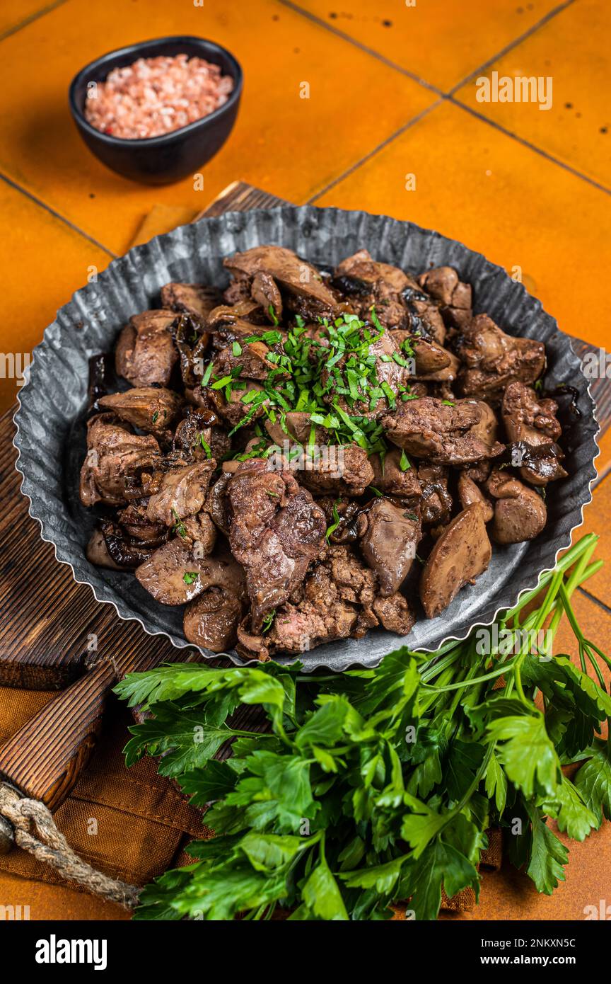 Roast chicken liver with onions and herb in a steel plate. Orange background. Top view. Stock Photo