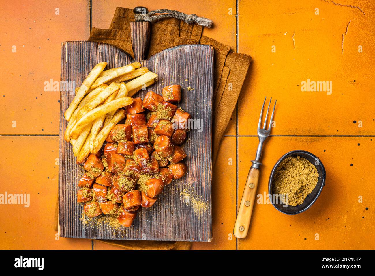 Curried sausage currywurst meal, curry wurst with french fry served on a wooden board. Orange background. Top view. Stock Photo