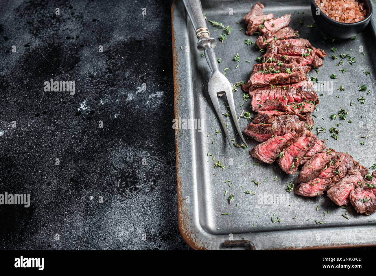 Grilled sliced Machete beef meat steak on steel tray with thyme. Black background. Top view. Copy space. Stock Photo