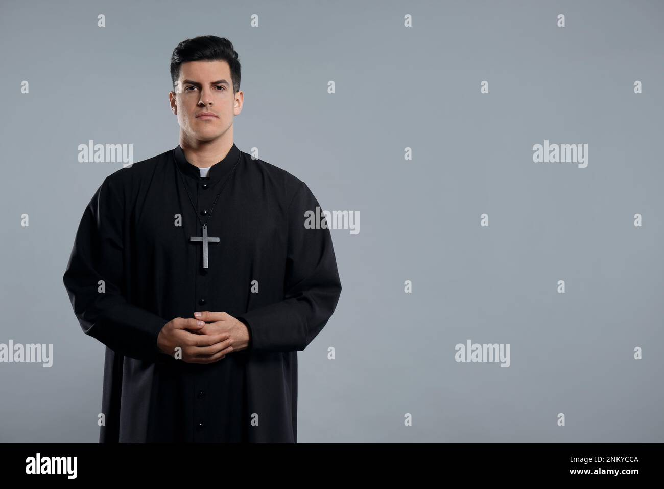 Priest wearing cassock with clerical collar on grey background. space for text Stock Photo