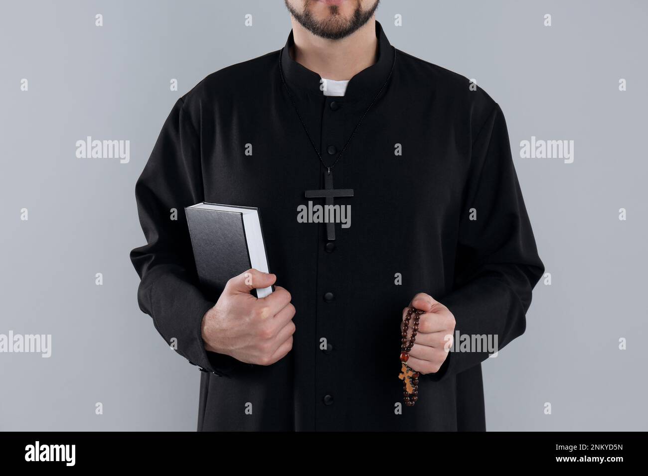 Priest with Bible and rosary beads on grey background, closeup Stock Photo