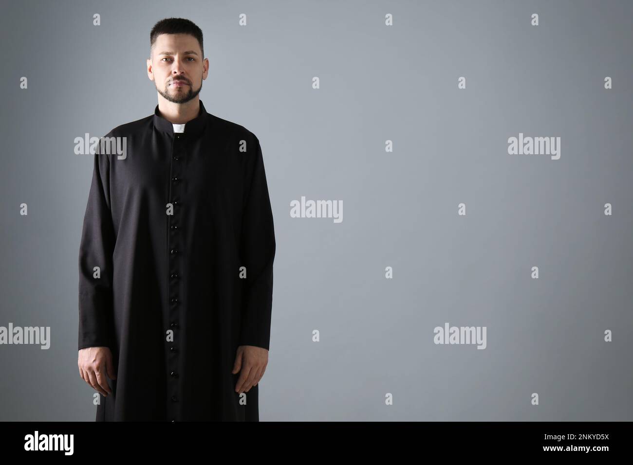 Priest wearing cassock with clerical collar on grey background, space for text Stock Photo