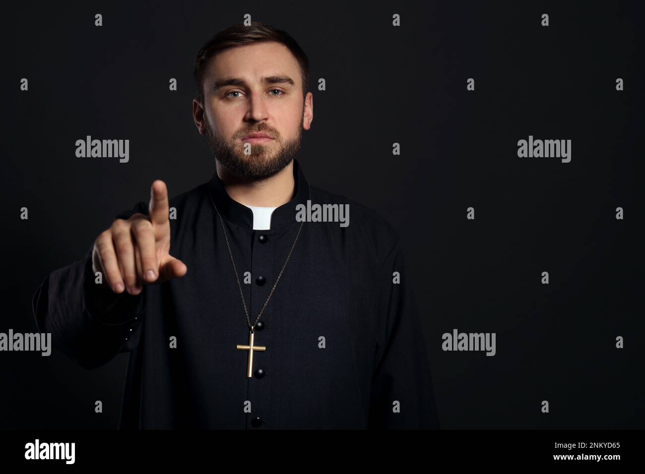 Priest wearing cassock with clerical collar on black background. Space for text Stock Photo