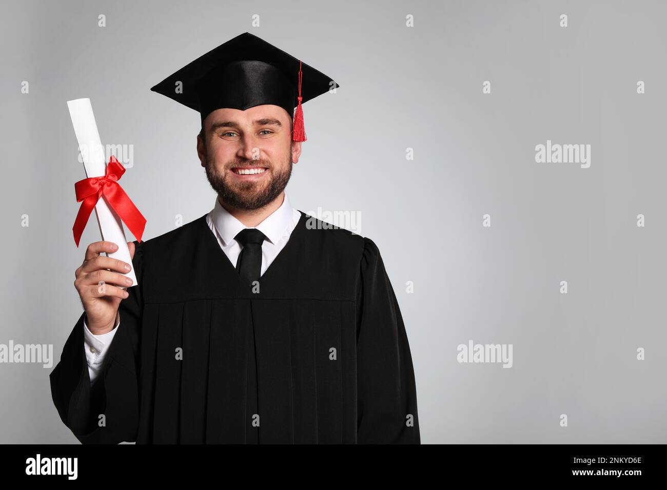 Happy student with graduation hat and diploma on grey background. Space ...