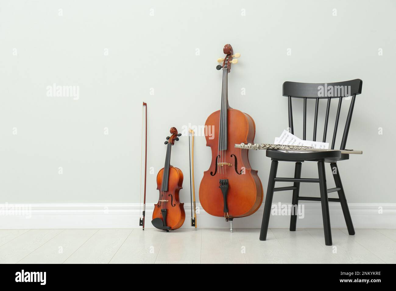 Stringed and wind musical instruments near white wall indoors, space