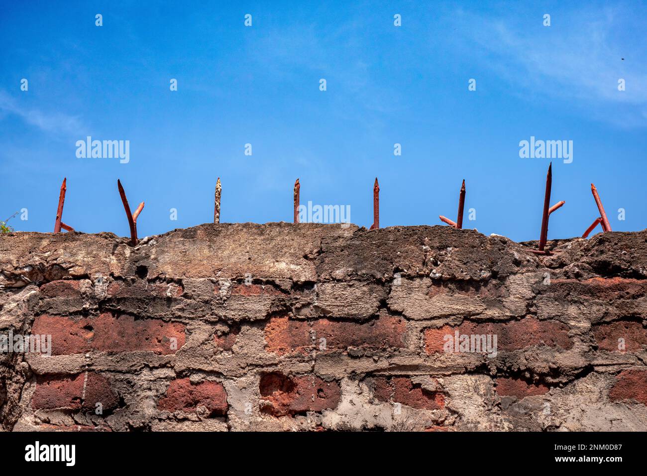 Red brick wall with sharp spikes on top. Clear blue sky with clouds. Theme for jail and freedom. Stock Photo
