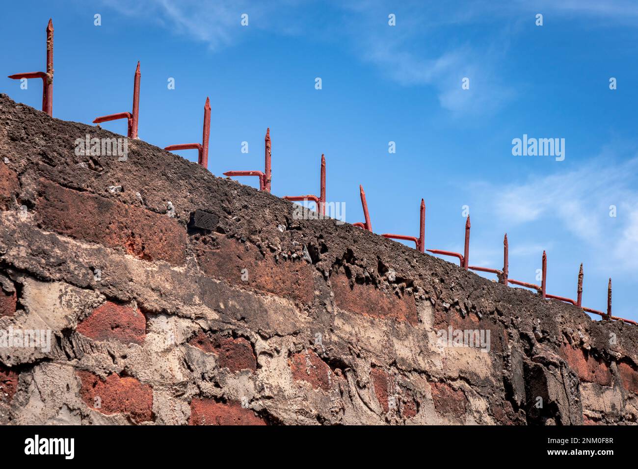 Red brick wall with sharp spikes on top. Clear blue sky with clouds. Theme for jail and freedom. Stock Photo