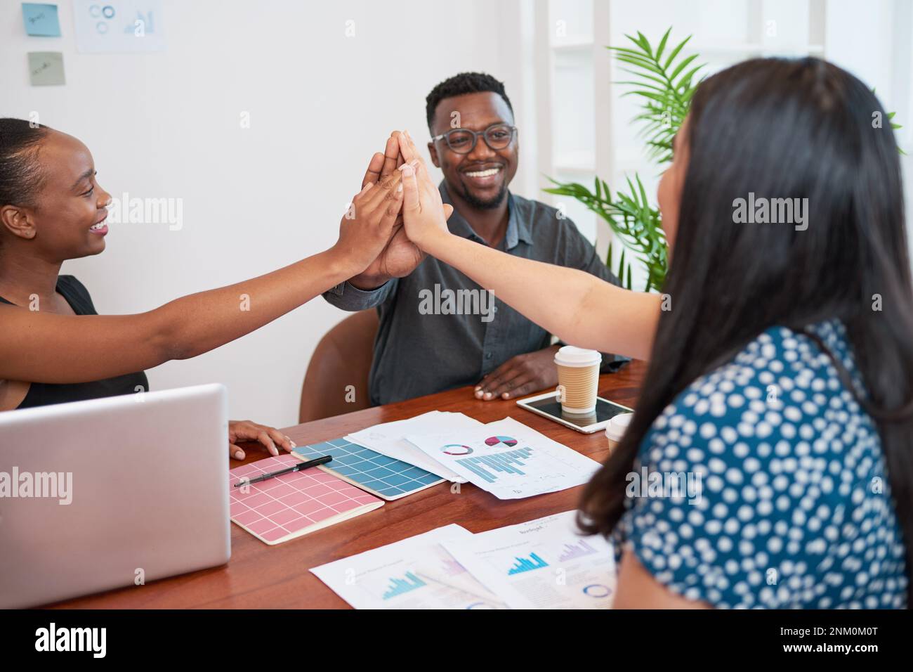 Diverse team give each other high five during boardroom meeting ...
