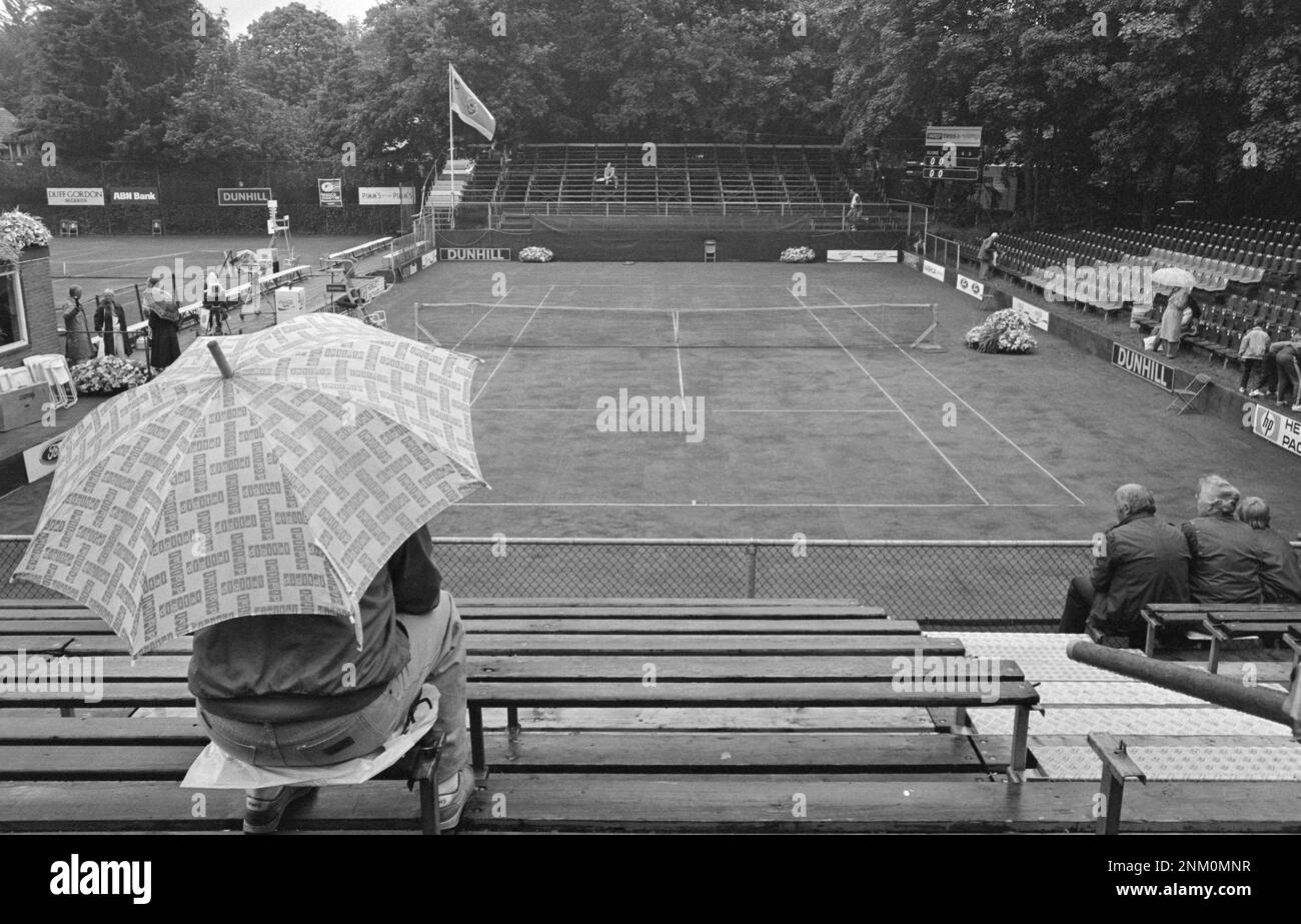 Rain during tennis match at Melkhuisje; man with umbrella in the stands ca. 1985 Stock Photo