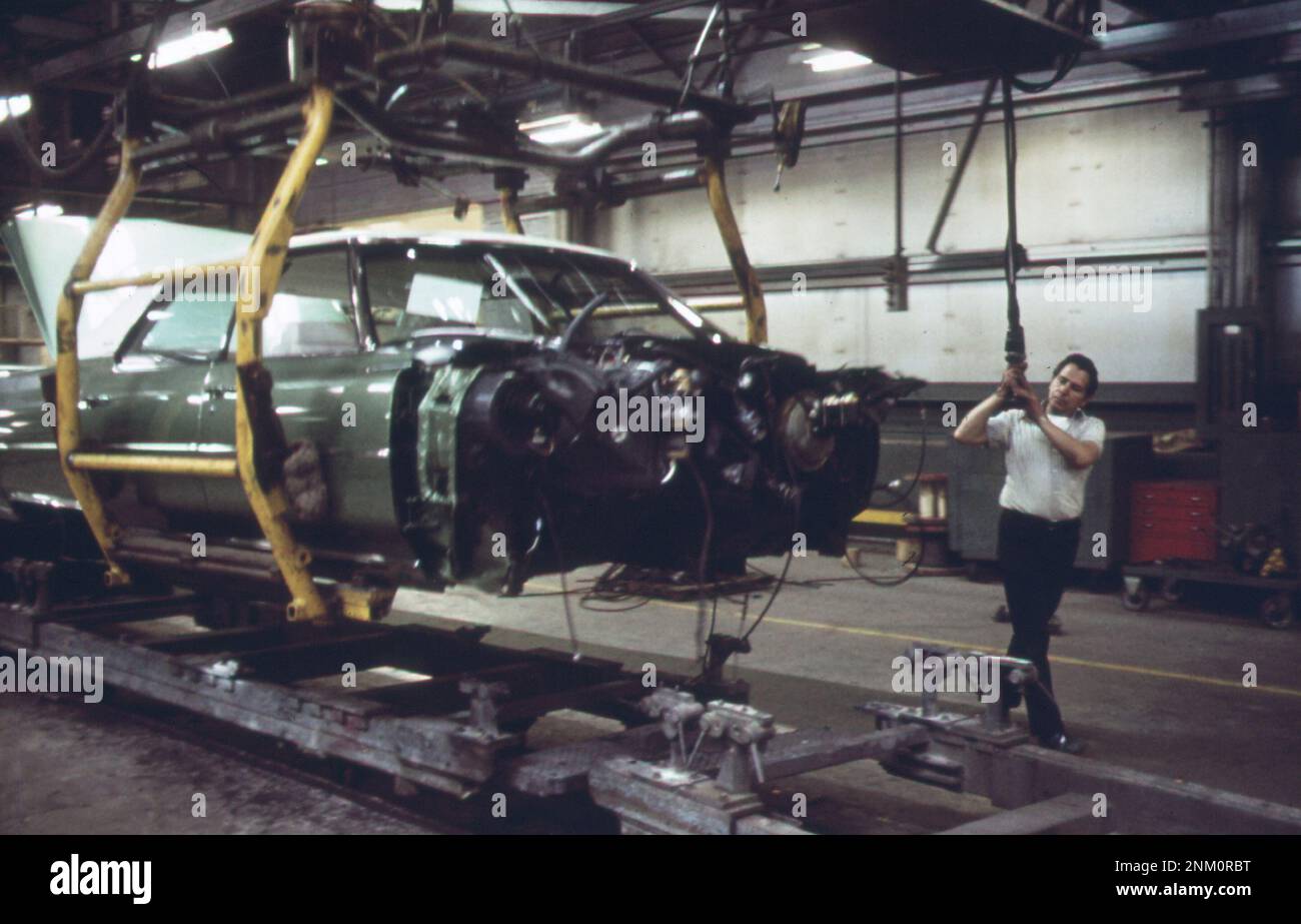 1970s America: On the Cadillac assembly line--wiring is complete on this body, and now the worker will 'drop' it through a hole in the floor to the main assembly line ca. 1973 Stock Photo