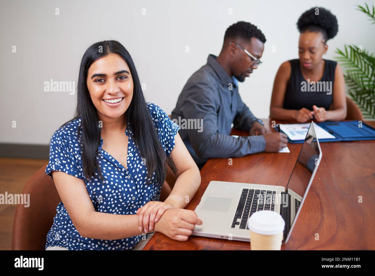 Indian business woman sits at conference table with colleagues, using laptop Stock Photo
