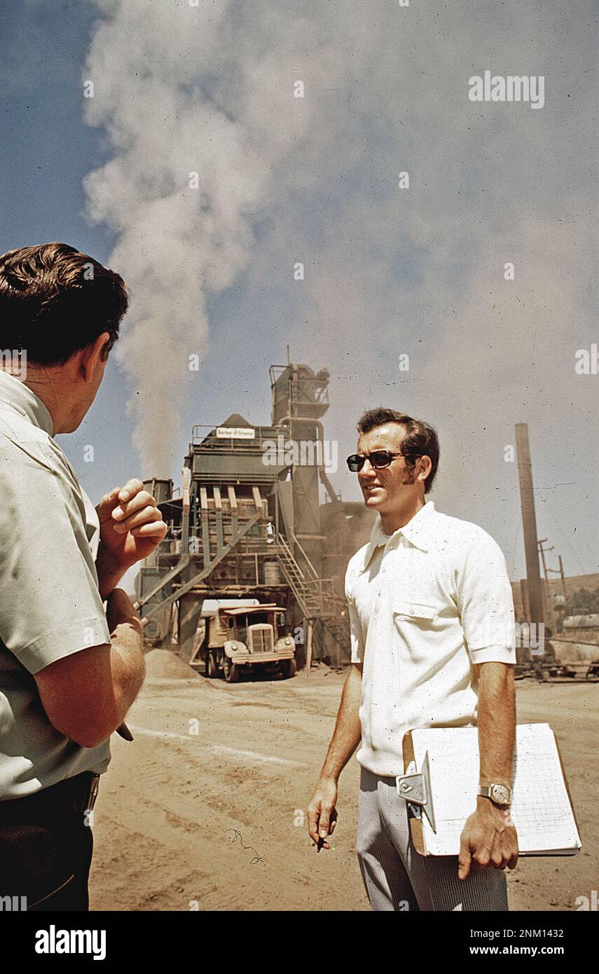 1970s United States:  Lou Dooley, registered sanitarian with air pollution control board, talks with the owner of an asphalt batch plant  ca.  1972 Stock Photo